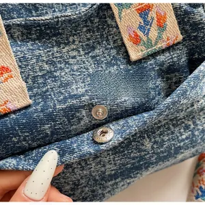 Detail of blue denim tote featuring silver metal snaps and colorful floral embroidery