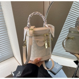 Detail of a beige bucket bag with woven texture, silk scarf handle, and mirror reflection