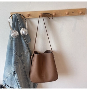 Detailed view of brown litchi leather bucket bag hanging on a wooden wall hook