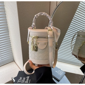 Detailed shot of beige leather bucket bag featuring woven pattern and silk scarf handle