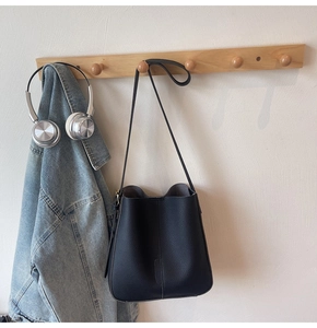 Close-up of black leather bucket bag on wood hook with denim jacket and headphones