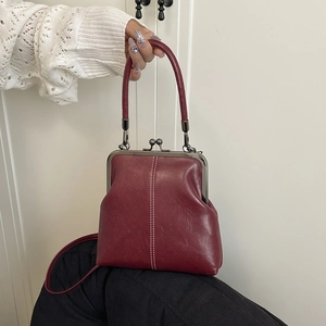 Close-up of retro burgundy shell bag with white stitching and vintage metal clasp