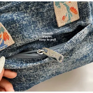 Detail of smooth silver butterfly zipper and floral embroidery on denim tote bag