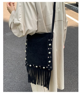 Detail of black suede crossbody bag with silver studs and long fringe tassels