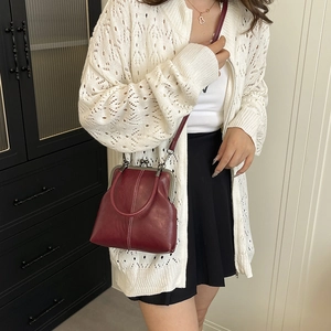 Detail view of burgundy leather crossbody bag with white stitching and metal clasp on model