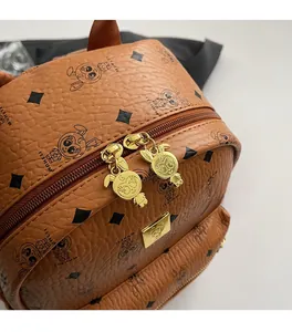 Detail of smooth gold cartoon zippers and logo plate on brown pebbled leather backpack