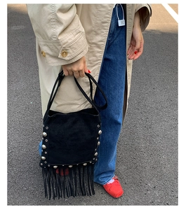 Street style view of a black suede crossbody bag with silver studs and long tassels