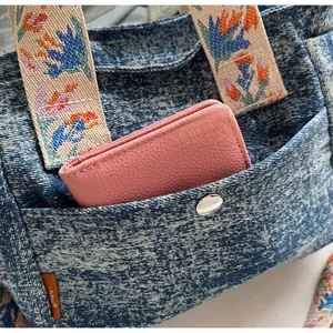 Detail of denim tote bag showing functional front pocket with a pink wallet inside