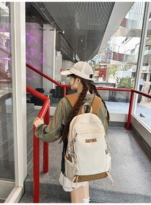 Side view of a beige and brown large capacity backpack worn by a model in a stairwell