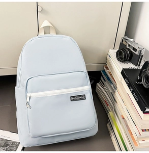 Close-up of light blue college backpack featuring front zip pocket and branded woven patch