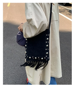 Street style shot of a black suede bag with silver studs and long leather tassels