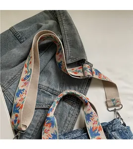Detail showing embroidered floral strap on denim tote bag with silver metal buckles