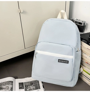 Detail of light blue backpack featuring brand patch, front zipper, and side pocket storage