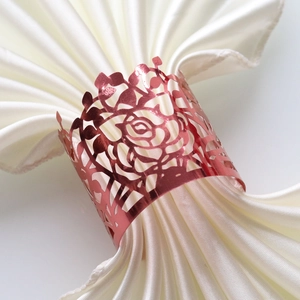 Detail of rose gold laser-cut floral napkin ring on a white silk cloth for parties