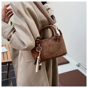 Dettaglio borsa scamosciata marrone scuro con manico annodato e ciondolo boho a perle