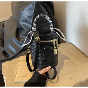 Detail of black woven bucket bag with gold hardware and geometric scarf handle