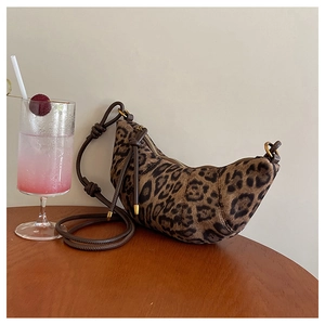 Dettaglio borsa croissant leopardata con tracolla a nodo su un tavolo di legno scuro