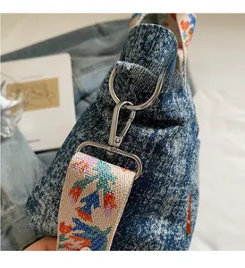 Detail of silver hardware and embroidered floral strap on blue denim crossbody bag
