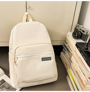 Close-up of ivory nylon backpack front pocket and logo patch with books background