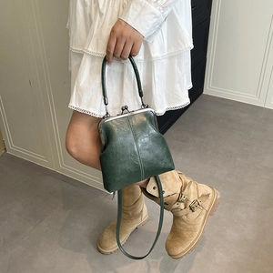 Model wearing a dark green vintage shell-style crossbody bag with metallic clasp and handle
