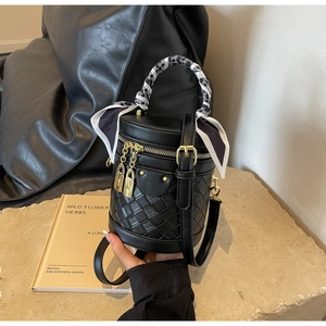 Detail of black cylinder bucket bag featuring woven leather texture and a gold padlock