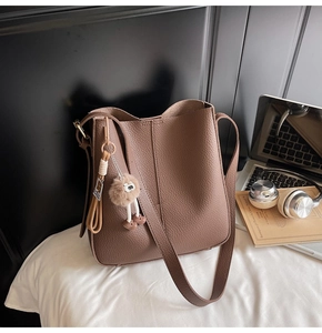 Brown lychee leather bucket bag with plush charm on a clean white bedding background