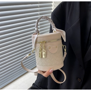Detail of cream bucket bag showing woven leather texture, gold padlock and silk scarf handle