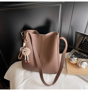 Detailed view of brown litchi grain leather bucket bag with cute fur ball charm pendant