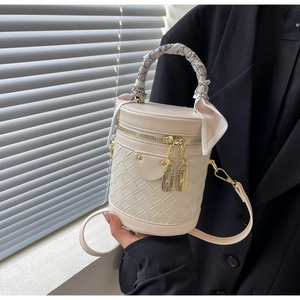Detail of cream woven bucket bag featuring silk scarf handle and golden hardware