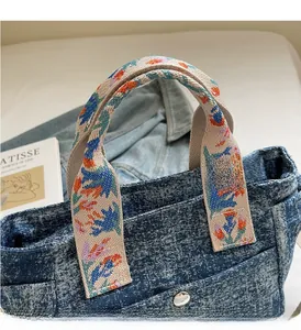 Detail of blue denim tote bag featuring colorful floral embroidered handles and metal hardware