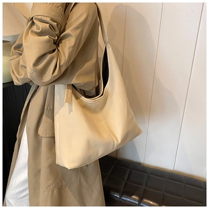 Sac hobo minimaliste en toile crème avec large bandoulière porté par un mannequin chic