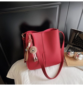 Detail view of red lychee textured tote bag with cute brown plush charm and shoulder strap