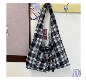 Detail of checkered tote bag with bow accent and leather tag on shoulder strap
