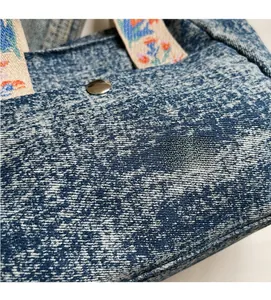 Detail of denim tote bag featuring floral embroidered handles and silver metal button