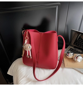Detail of red pebbled leather bucket bag with plush monster charm on white bedding