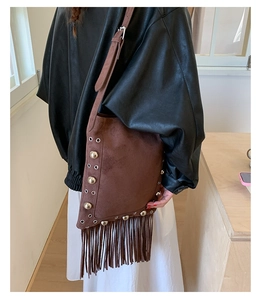 Detail of dark brown suede shoulder bag featuring bohemian metal rivets and long tassels
