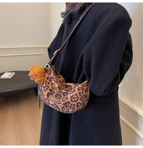 Detail of leopard print hobo bag with leather strap and plush dog charm on black coat