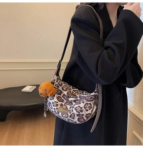 Detail of leopard print crescent bag with brown strap and teddy bear charm on black coat