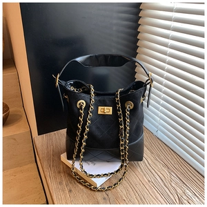 Detail of black quilted bucket bag featuring a gold twist lock and metal chain strap