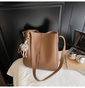 Close-up of tan lychee grain leather bucket bag with cute plush eye charm and shoulder strap