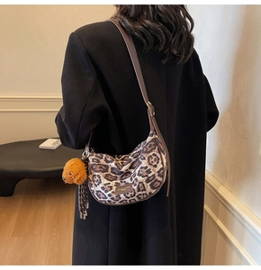Close-up of leopard print crescent bag with leather strap and cute plush puppy charm