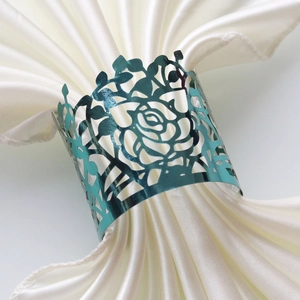 Macro shot of teal hollow-out rose napkin ring on a white satin cloth for table decor