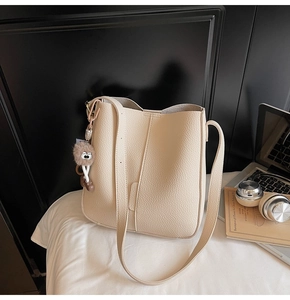 Close-up of beige pebble leather bucket bag with cute monster charm and long strap