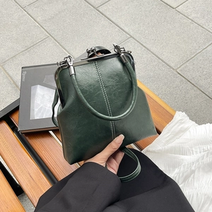 Detailed view of green leather shell bag with vintage metal clasp and top handles