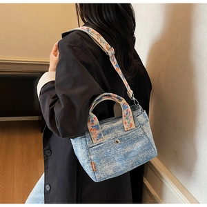 Macro detail of denim tote featuring floral embroidery on the handle and strap