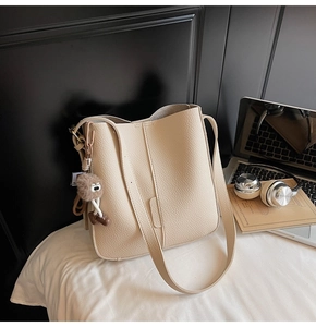 Close-up of off-white lychee grain leather bucket bag with a cute brown plush monster charm