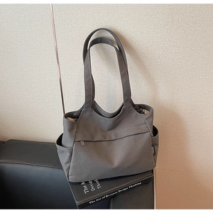 Dettaglio della borsa tote in tela grigio scuro con tasca a zip e logo laterale in tessuto