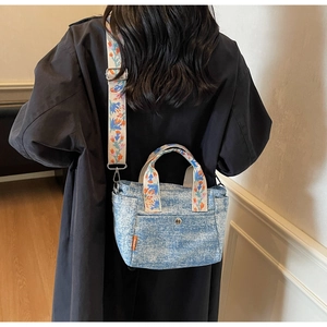 Detail of floral embroidery on light blue denim tote bag with metal buckle and orange label