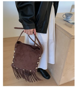 Detail of brown suede bucket bag with metallic rivets and fringe tassels in retro style