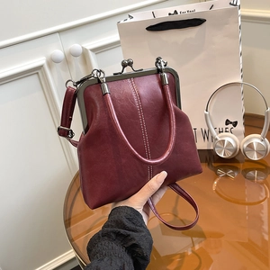 Detail of vintage burgundy leather shell bag with metal clasp and double stitching
